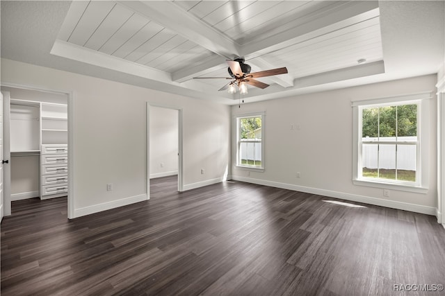 unfurnished bedroom featuring dark wood-style floors, baseboards, a tray ceiling, a spacious closet, and beamed ceiling