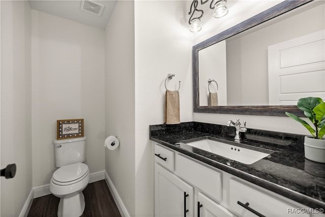 half bath featuring visible vents, toilet, wood finished floors, baseboards, and vanity