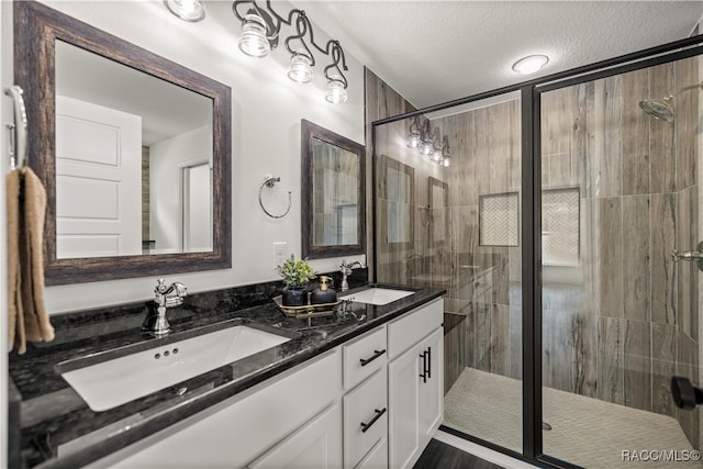 full bath featuring double vanity, a shower stall, a textured ceiling, and a sink