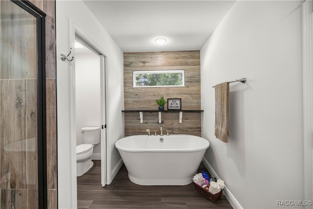 bathroom featuring wood finished floors, baseboards, a soaking tub, wood walls, and toilet