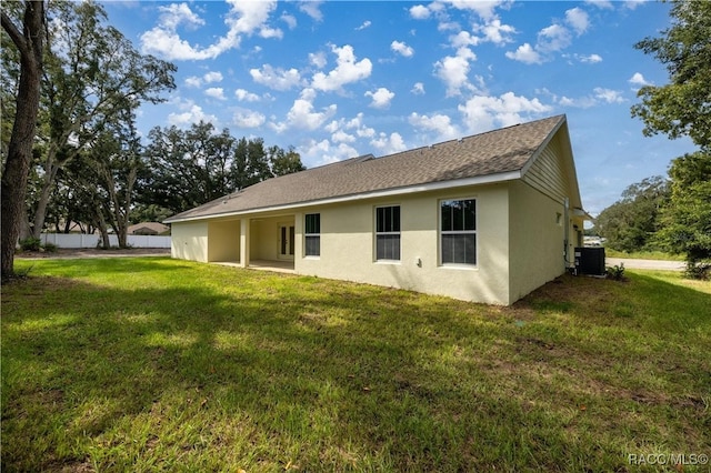 back of house featuring fence, roof with shingles, a yard, stucco siding, and central air condition unit