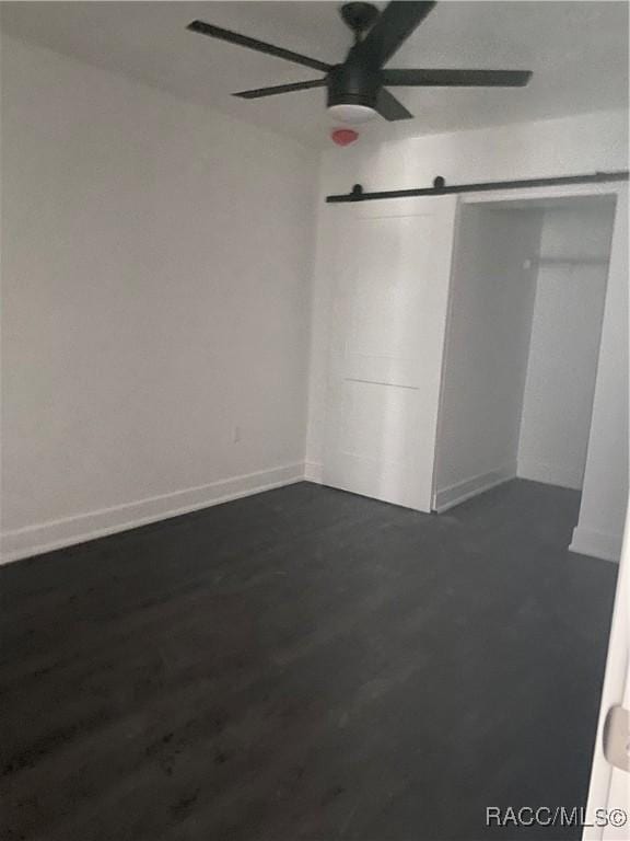 unfurnished bedroom featuring ceiling fan, a barn door, and dark hardwood / wood-style flooring