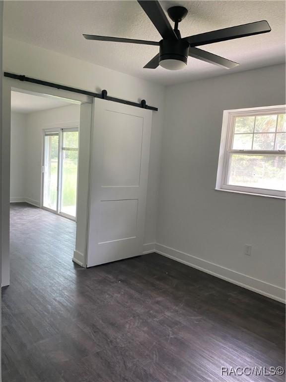 unfurnished room with a barn door, ceiling fan, and dark hardwood / wood-style flooring