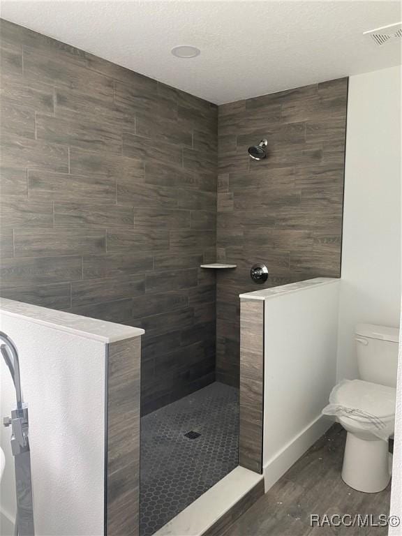 bathroom featuring a tile shower, toilet, and hardwood / wood-style flooring