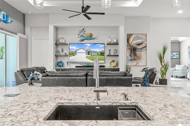 kitchen with ceiling fan, light stone counters, and sink