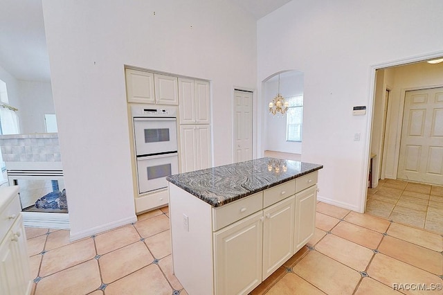 kitchen featuring dark stone countertops, light tile patterned flooring, a center island, and double oven