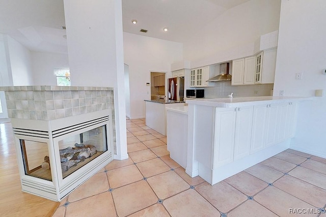 kitchen featuring white cabinetry, kitchen peninsula, tasteful backsplash, appliances with stainless steel finishes, and wall chimney exhaust hood