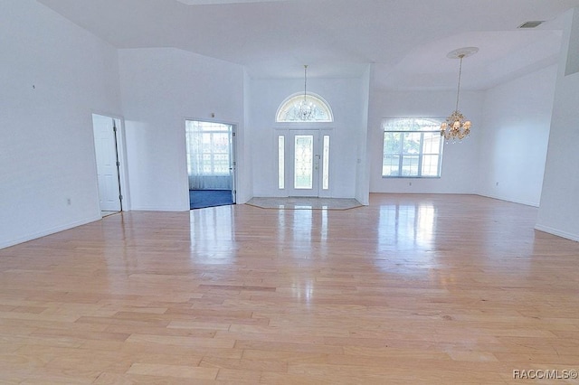 empty room with a towering ceiling, a chandelier, and light hardwood / wood-style floors