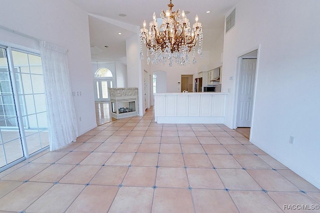 unfurnished living room with a notable chandelier, light tile patterned floors, and a high ceiling