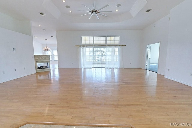 unfurnished living room with a high ceiling, a multi sided fireplace, ceiling fan, light hardwood / wood-style floors, and a raised ceiling