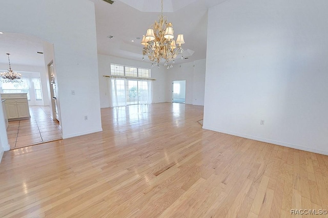 empty room with light hardwood / wood-style flooring, a high ceiling, and a notable chandelier