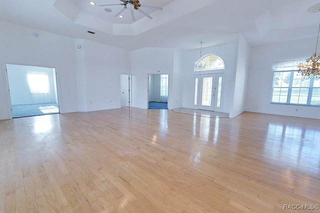 unfurnished living room featuring ceiling fan with notable chandelier, light hardwood / wood-style flooring, a high ceiling, and a tray ceiling