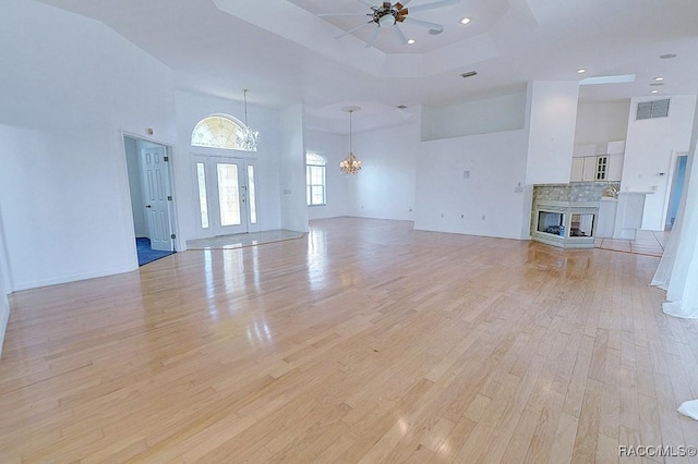 unfurnished living room featuring a multi sided fireplace, ceiling fan with notable chandelier, light hardwood / wood-style floors, a raised ceiling, and a high ceiling