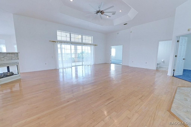 unfurnished living room featuring ceiling fan, light wood-type flooring, a high ceiling, and a raised ceiling