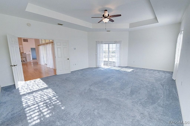 carpeted spare room with ceiling fan and a raised ceiling