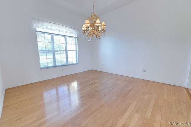 spare room with light wood-type flooring, vaulted ceiling, and a notable chandelier