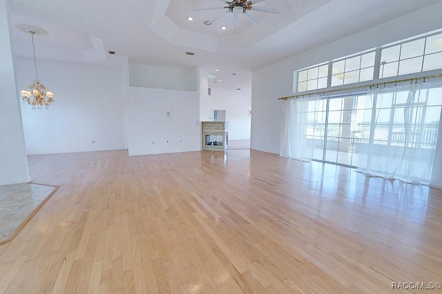 unfurnished living room featuring light hardwood / wood-style flooring, a multi sided fireplace, ceiling fan with notable chandelier, a raised ceiling, and a high ceiling