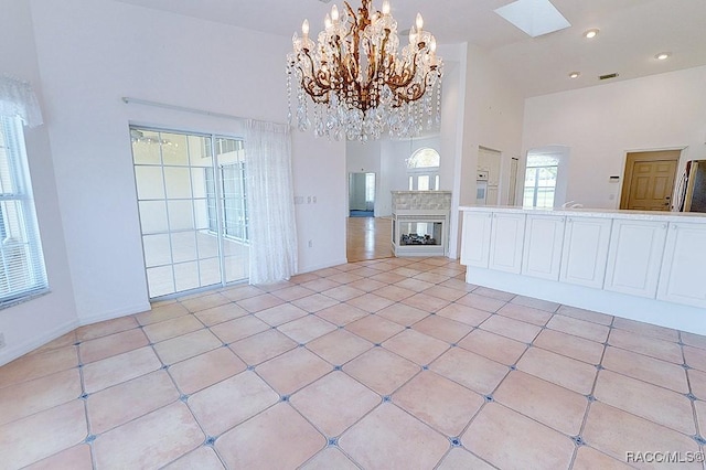 unfurnished living room featuring a skylight, a towering ceiling, a chandelier, and light tile patterned floors