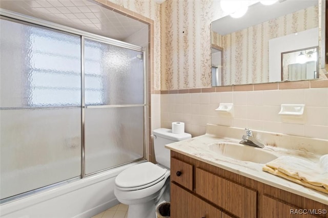 full bathroom with combined bath / shower with glass door, tile patterned floors, toilet, vanity, and tile walls