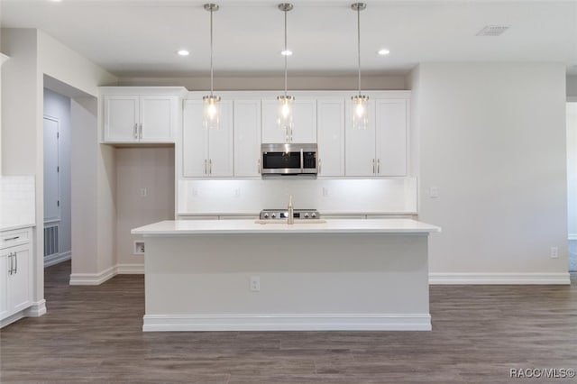 kitchen with decorative light fixtures, a center island with sink, and white cabinetry