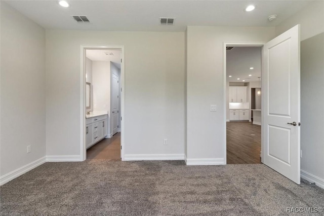 unfurnished bedroom with ensuite bath and dark carpet