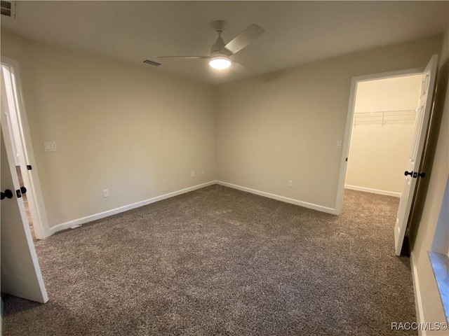 unfurnished bedroom featuring a spacious closet, a closet, ceiling fan, and dark colored carpet