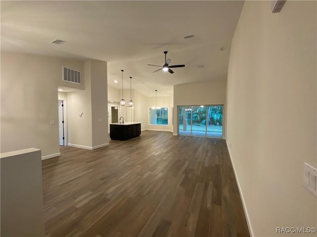 unfurnished living room featuring a high ceiling, ceiling fan with notable chandelier, dark hardwood / wood-style floors, and sink