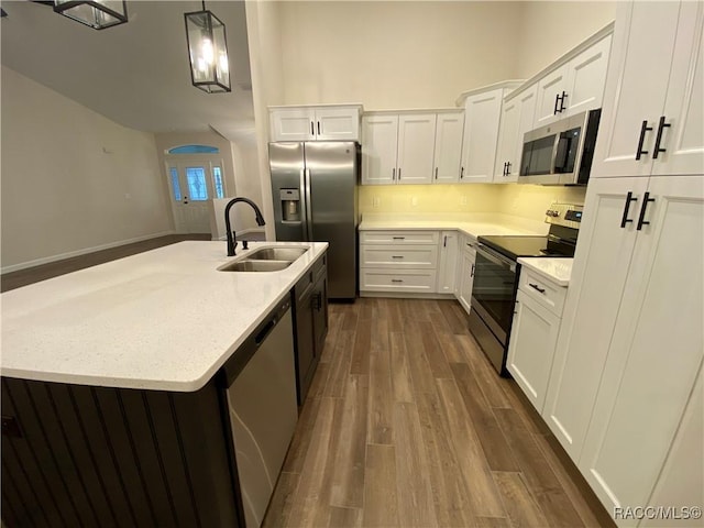 kitchen with stainless steel appliances, a kitchen island with sink, dark hardwood / wood-style floors, white cabinetry, and hanging light fixtures