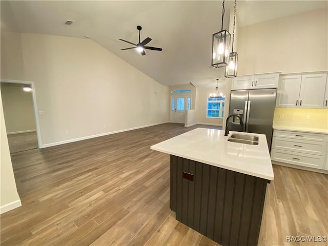 kitchen with lofted ceiling, hanging light fixtures, light hardwood / wood-style flooring, an island with sink, and white cabinetry