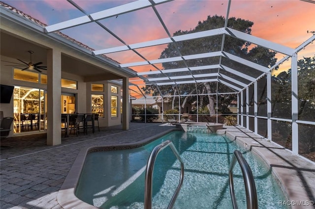 pool at dusk with a patio, ceiling fan, and glass enclosure