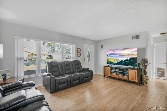 living room with baseboards, a textured ceiling, visible vents, and light wood-style floors