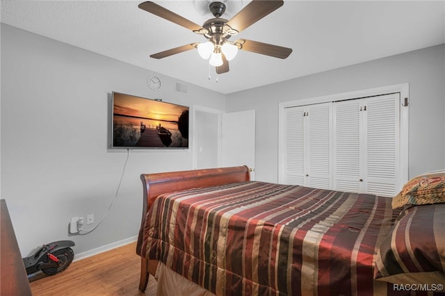 bedroom with wood finished floors, a ceiling fan, visible vents, baseboards, and a closet