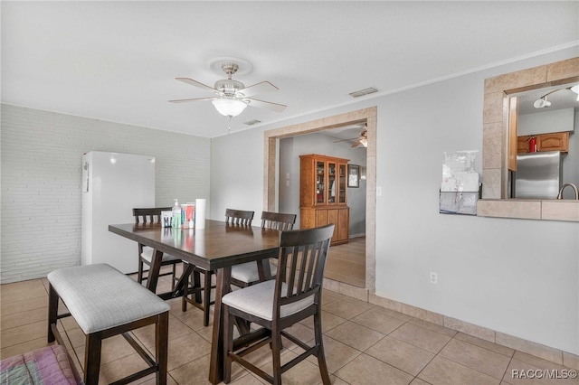 dining room with baseboards, visible vents, a ceiling fan, brick wall, and light tile patterned flooring