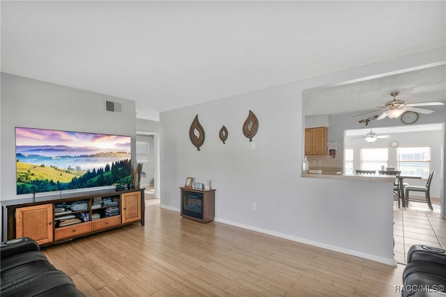 living room with light wood finished floors, baseboards, visible vents, and ceiling fan