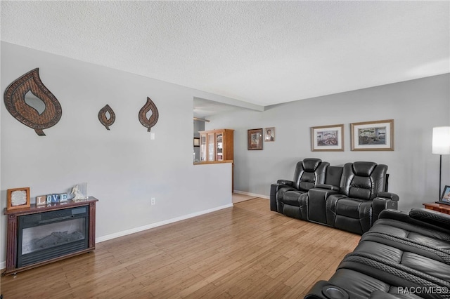 living room featuring hardwood / wood-style flooring, baseboards, a textured ceiling, and a glass covered fireplace