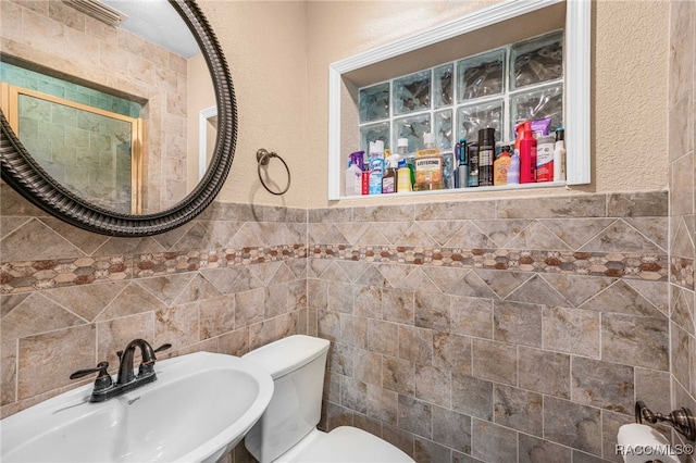 bathroom featuring toilet, a wainscoted wall, tile walls, and a sink