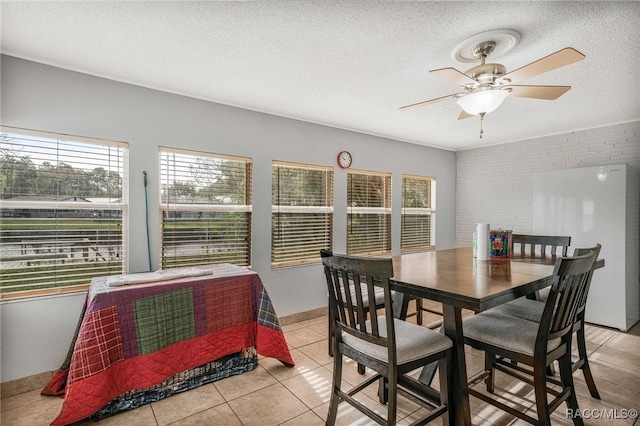 dining area with a textured ceiling, ceiling fan, light tile patterned floors, brick wall, and baseboards