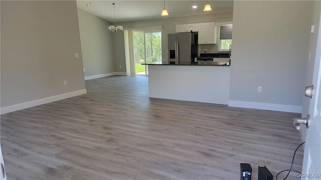 kitchen with stainless steel refrigerator with ice dispenser, decorative light fixtures, an inviting chandelier, light hardwood / wood-style flooring, and white cabinetry