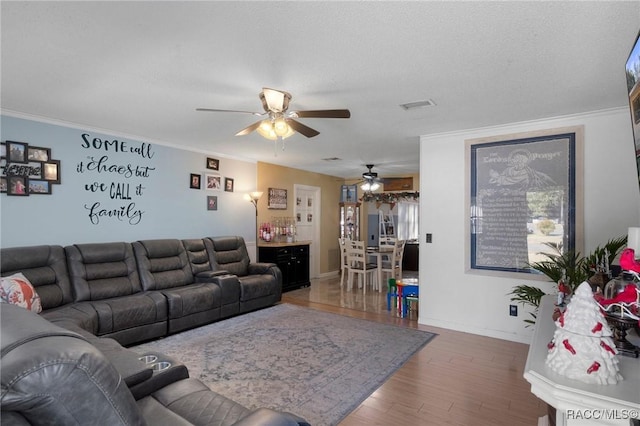 living area featuring visible vents, a textured ceiling, wood finished floors, crown molding, and baseboards