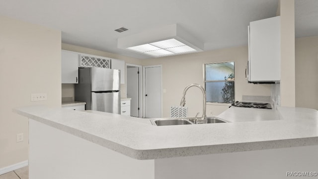 kitchen with kitchen peninsula, white cabinetry, stainless steel refrigerator, and sink