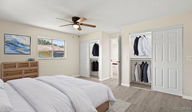 bedroom featuring ceiling fan, two closets, a textured ceiling, and light hardwood / wood-style flooring