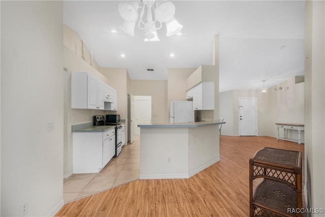 kitchen featuring stainless steel electric stove, white cabinets, light wood-type flooring, white fridge, and vaulted ceiling