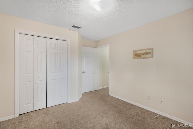 unfurnished bedroom featuring light colored carpet, a textured ceiling, and a closet