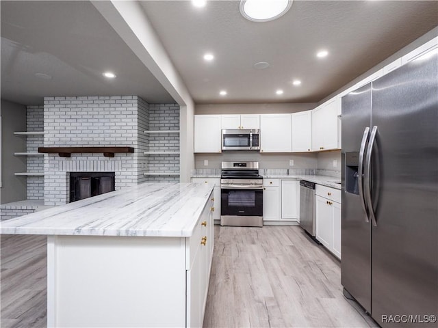 kitchen featuring light hardwood / wood-style floors, a brick fireplace, white cabinets, stainless steel appliances, and light stone counters