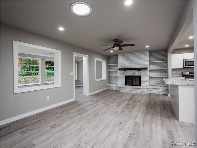 unfurnished living room featuring ceiling fan, brick wall, light hardwood / wood-style flooring, and a fireplace