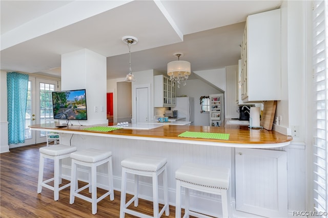 kitchen featuring dark wood-type flooring, an inviting chandelier, kitchen peninsula, white fridge, and a breakfast bar area