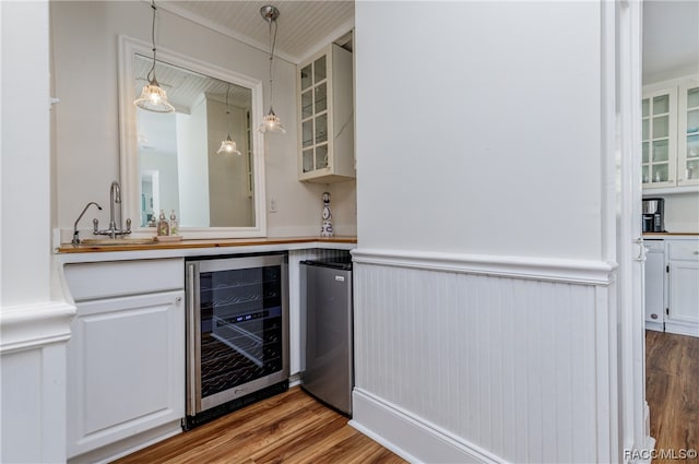 bar with hanging light fixtures, wood-type flooring, white cabinetry, and beverage cooler