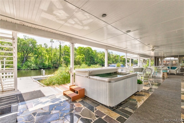 unfurnished sunroom featuring ceiling fan, a water view, and a hot tub