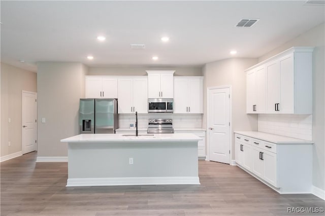 kitchen with light hardwood / wood-style floors, white cabinetry, an island with sink, and appliances with stainless steel finishes