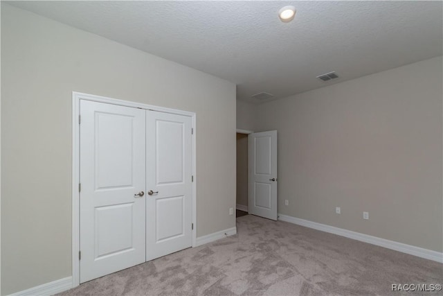 unfurnished bedroom with light colored carpet, a closet, and a textured ceiling